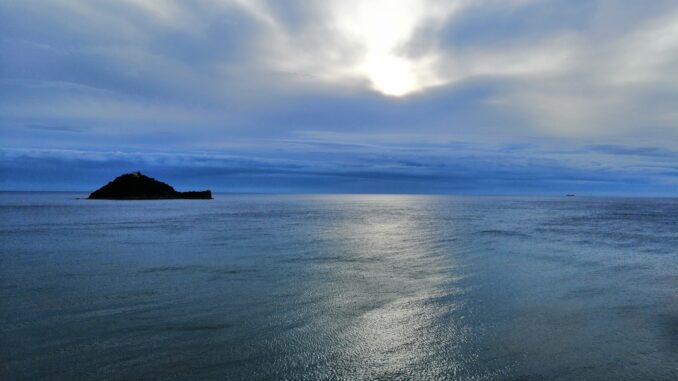 un cielo plumbeo sul mare quieto della Liguria e l'Isola Gallinara in lontananza