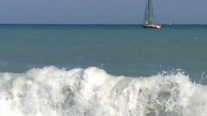Albenga con vista sui flutti del mare e una barca a vela che si allontana dalla spiaggia nella foto di Roberto Ruaro