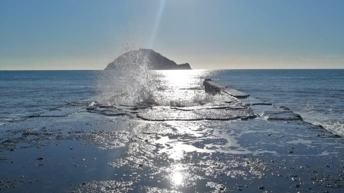 Alba di mare le onde si rifrangono sul molo ad Albenga in lontananza l'Isola Gallinara nella foto di Roberto Ruaro