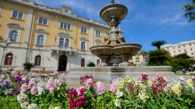 una vista di una parte della piazza, con la fontana in primo piano e più in lontananza la facciata del Palazzo Comunale
